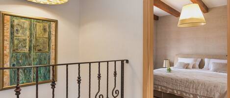 A bedroom with a bed, a bedside table, and a lamp. There is a painting on the wall and a window with curtains.