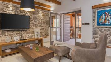 A living room with a stone wall, a flat-screen TV, a wooden coffee table, a grey sofa, and a painting of sailboats.