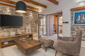 Un salon avec un mur en pierre, un téléviseur à écran plat, une table basse en bois, un canapé gris et un tableau représentant des voiliers.