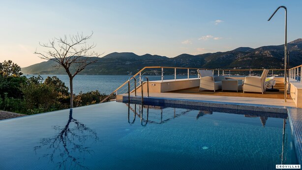 A pool with clear blue water, a wooden deck, and a view of mountains and a body of water. - Soul Stella in Kor ula (Korčula)