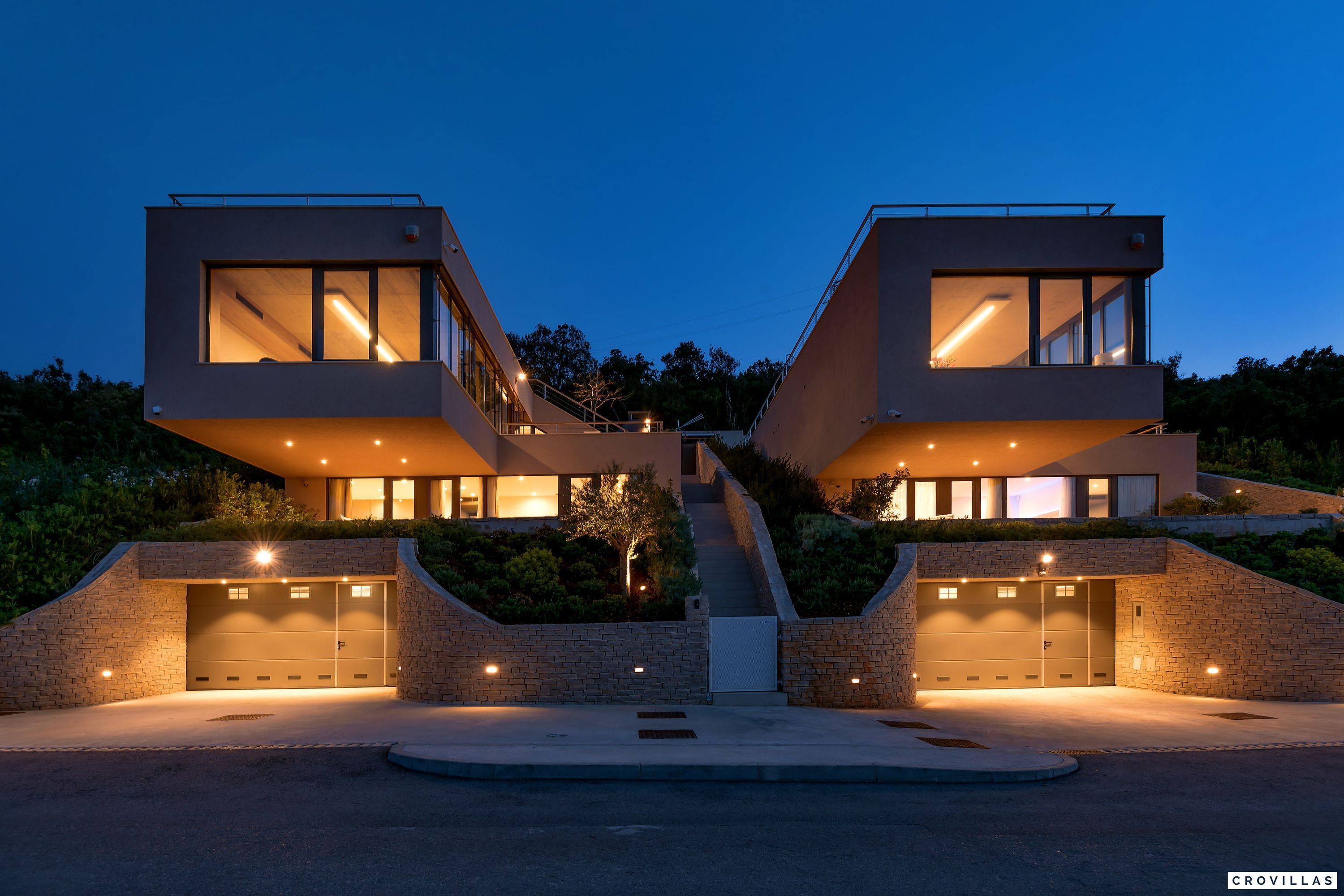 Una casa moderna de dos pisos amb un garatge, una escala que condueix al pis superior i una entrada ben il·luminada.