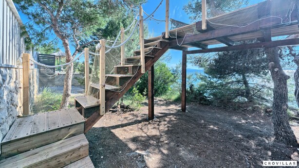 A wooden outdoor staircase leading to a wooden deck, surrounded by trees and a clear sky. - Treehouse in Murter With 1 Bedrooms and 1 Bathrooms (Tisno)