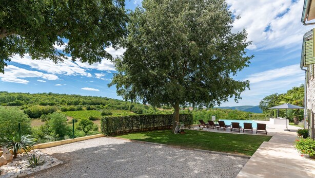 A spacious outdoor area with a gravel patio, a grassy lawn, and a large tree providing shade. - Zvonar in Rakotule With 3 Bedrooms and 3 Bathrooms (Karojba)