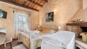 A bedroom with a bed, a desk, a chair, a window with curtains, a painting on the wall, and a fireplace. - Zvonar in Rakotule With 3 Bedrooms and 3 Bathrooms (Karojba)
