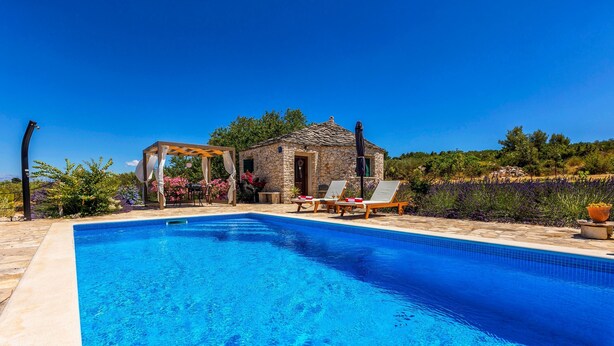 A clear blue swimming pool with lounge chairs and a stone building in the background. - Magical Island in Mirca (Supetar)