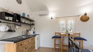 A compact kitchen with wooden cabinets, a black countertop, and a dining area with a table and chairs. - Magical Island in Mirca (Supetar)