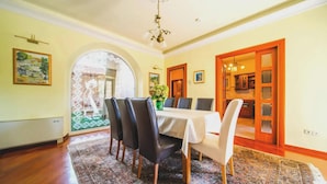 Een eetkamer met een gedekte tafel voor zes personen, een kroonluchter en uitzicht door een boogvormige deuropening.