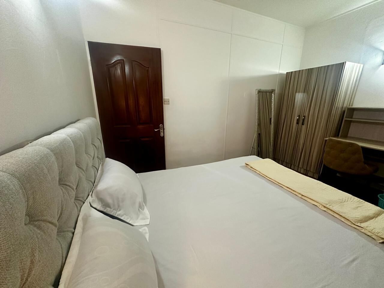 A bedroom with a bed, a wooden door, a wardrobe, and a chair.
