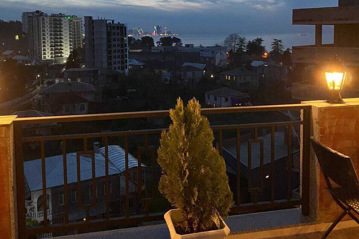 Un balcón con una planta en maceta, una silla y vista a un paisaje urbano al anochecer.