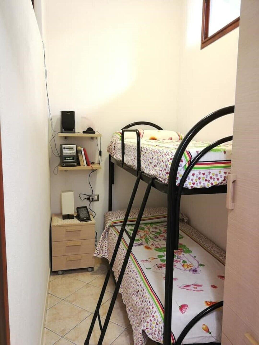 A small, compact room with bunk beds, a desk with a computer and books, and a shelf with electronic devices.