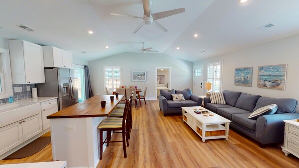 A spacious living area with a wooden dining table, grey sofas, and a ceiling fan.