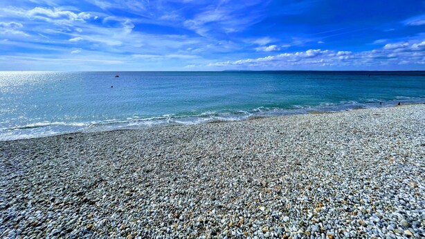 A pebbled beach with a clear sky and calm sea.