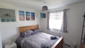 A bedroom with a wooden bed, a nightstand, a radiator, a window with curtains, and wall art.