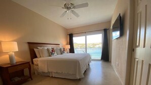 Une chambre à coucher comprenant un lit, une table de chevet, un ventilateur de plafond et une vue sur la mer par une grande fenêtre.