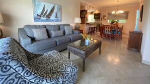 Un salon comprenant un canapé, un pouf à motifs, une table basse et un tableau représentant des voiliers.