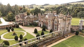 A large, historic castle with multiple towers, a well-maintained garden, and a bridge leading to the entrance. - World famous house in the beautiful Scottish Borders (Melrose)