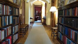A library with bookshelves on both sides, a central aisle, and a lamp on the right.