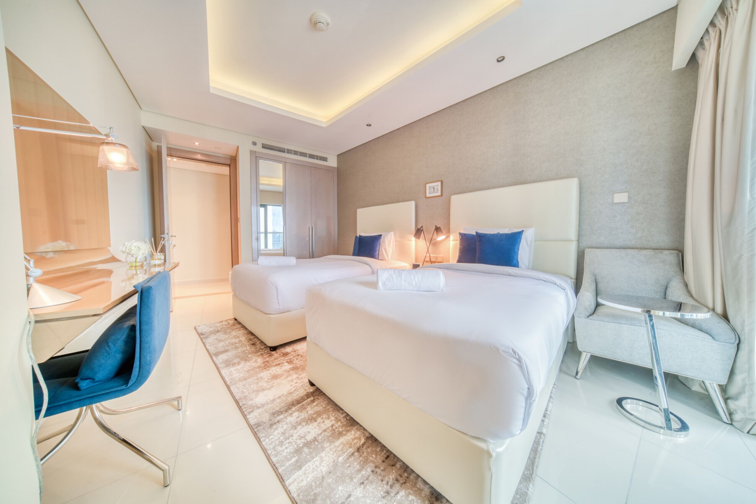Et moderne hotelværelse med to senge, et skrivebord, en stol og et lille bord.