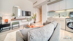 A modern living room with a grey sofa, a flat-screen TV, and a dining area with a table and chairs. - Picturesque Studio at Mesk 1 Midtown Dubai Production City by Deluxe Holiday Homes (Dubai)
