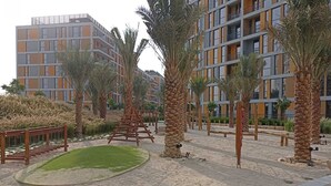 A modern building with multiple balconies and a landscaped area with palm trees and a wooden swing set. - Picturesque Studio at Mesk 1 Midtown Dubai Production City by Deluxe Holiday Homes (Dubai)