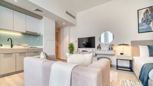 Una sala moderna con sofá, televisión y comedor, con una cocina al fondo.