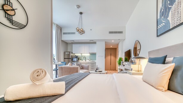 Una habitación de hotel moderna con una cama grande, un comedor y una cocina al fondo.