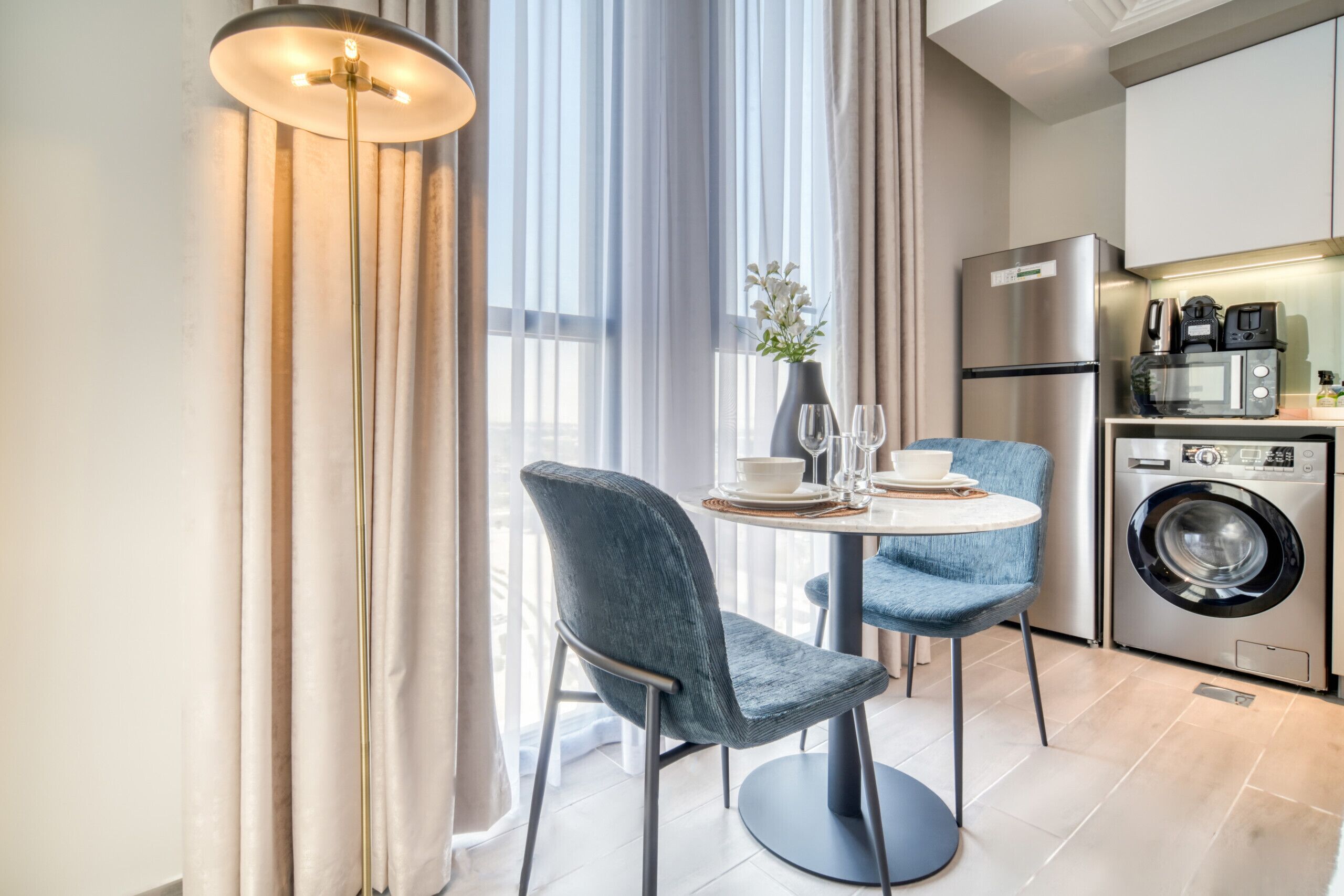 A modern kitchen with a washing machine, a refrigerator, and a dining area with a table and chairs.