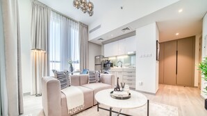 Una sala de estar moderna con un sofá beige, una mesa de centro redonda y una cocina al fondo.