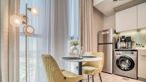 Una cocina moderna con lavadora integrada, una zona de comedor con dos sillas y un amplio ventanal con cortinas.