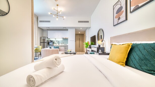 Una habitación de hotel moderna con una cama bien hecha, un área de comedor y una cocina al fondo.