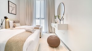 A modern bedroom with a large bed, a bedside lamp, a round mirror, and a neutral color scheme. - Harmonious 2BR w/ Assistant’s Room at Mesk 1 Midtown Dubai Production City by Deluxe Holiday Homes (Dubai)