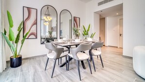 A modern dining area with a round table set for six, surrounded by grey upholstered chairs. There are three large mirrors on the wall, a potted plant, and a hanging light fixture. - Harmonious 2BR w/ Assistant’s Room at Mesk 1 Midtown Dubai Production City by Deluxe Holiday Homes (Dubai)