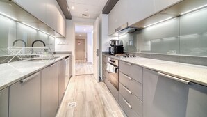 A modern kitchen with stainless steel appliances, grey cabinetry, and a light wood floor. - Harmonious 2BR w/ Assistant’s Room at Mesk 1 Midtown Dubai Production City by Deluxe Holiday Homes (Dubai)