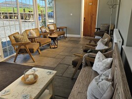 Una habitación con ventanas amplias, sillas de mimbre, un banco de madera y una mesa con una vela.