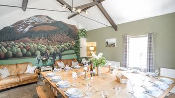 A dining area with a long wooden table set for a meal, a mural on the wall, and a cozy seating area with a leather couch.