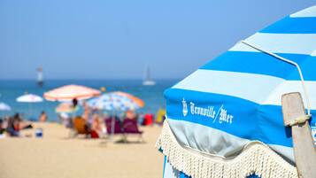 Una ombrel·la de platja amb la inscripció "Cronwell/Mer", una platja de sorra i persones al fons.