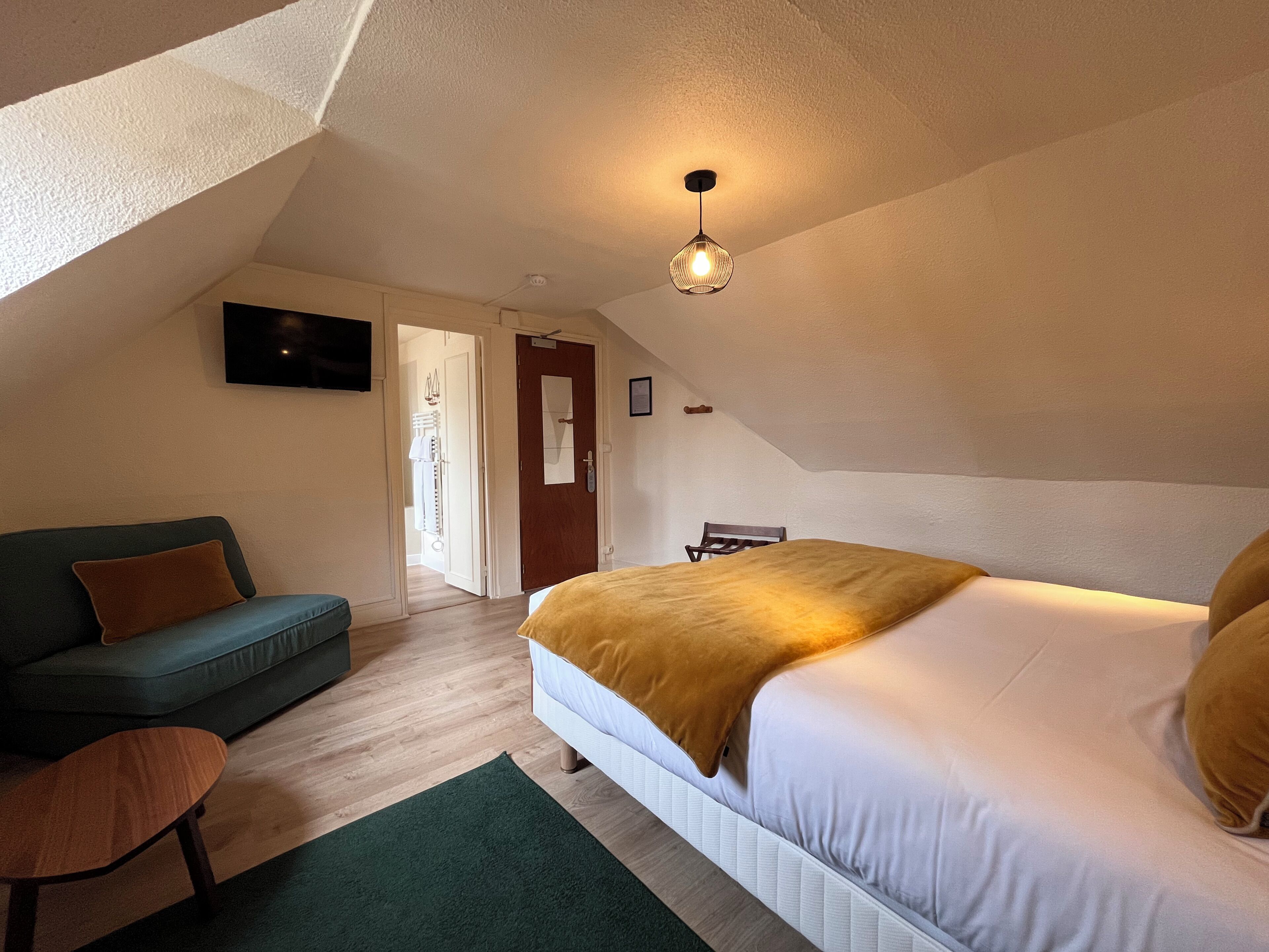 A bedroom with a bed, a sofa, a chair, a TV, and a door leading to another room.