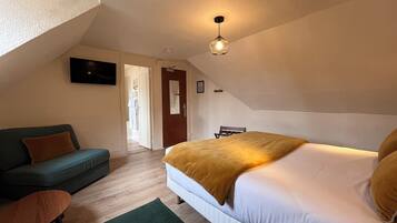 Une chambre à coucher comprenant un lit, un canapé, une chaise, un téléviseur et une porte donnant sur une autre pièce.