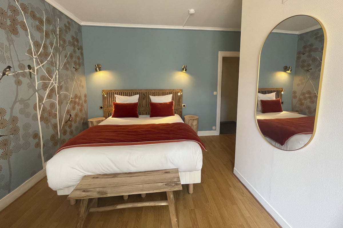 Een slaapkamer met een bed, een houten bankje, een spiegel en wandlampen.