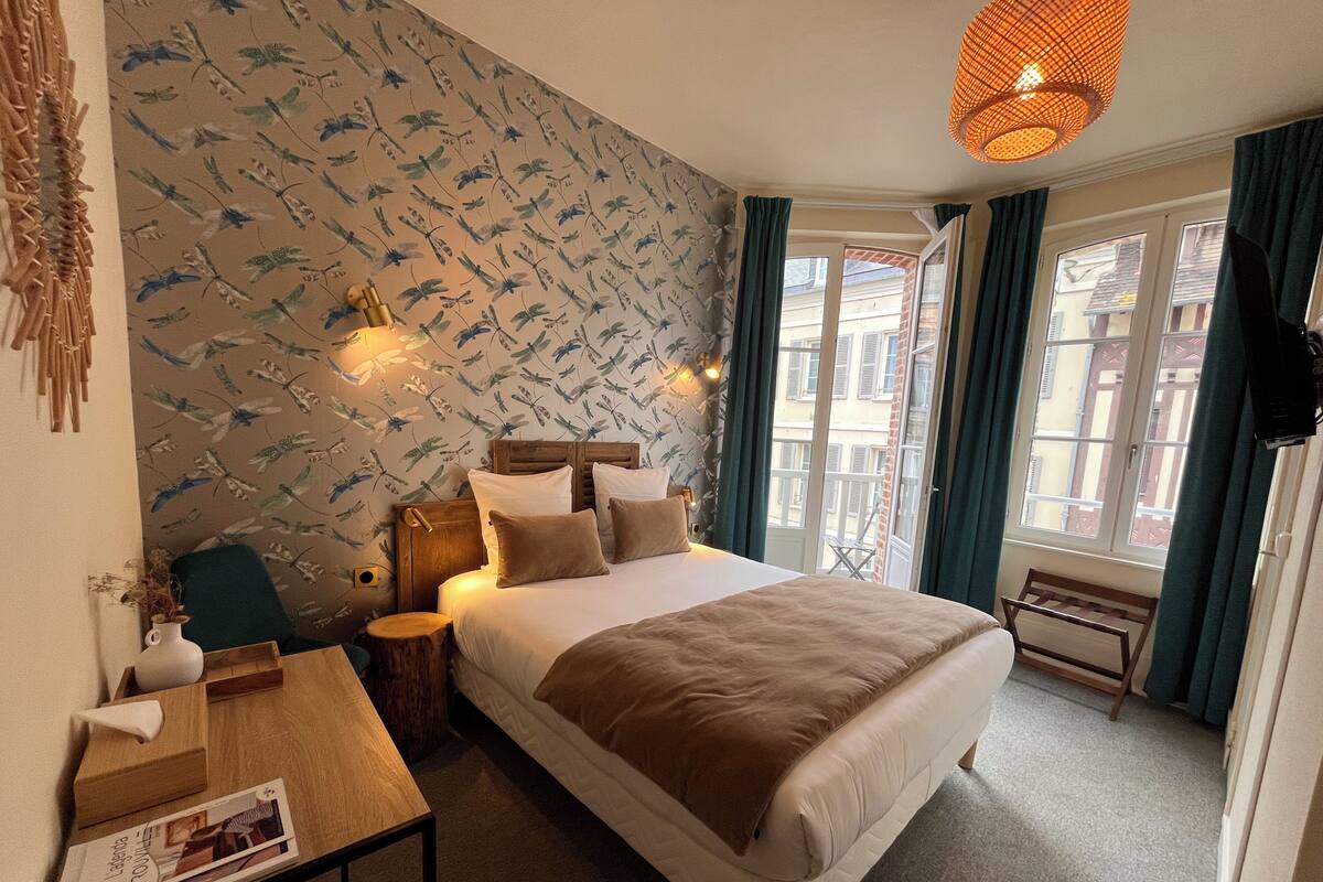 Een slaapkamer met een bed, nachtkastje, lamp en uitzicht.