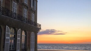 Un immeuble doté d’un balcon donnant sur une plage au coucher du soleil.