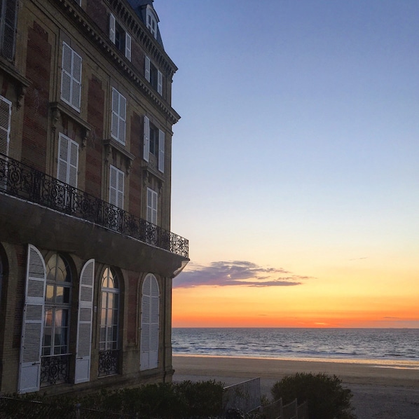 Un edificio con balcón que da a una playa al atardecer.