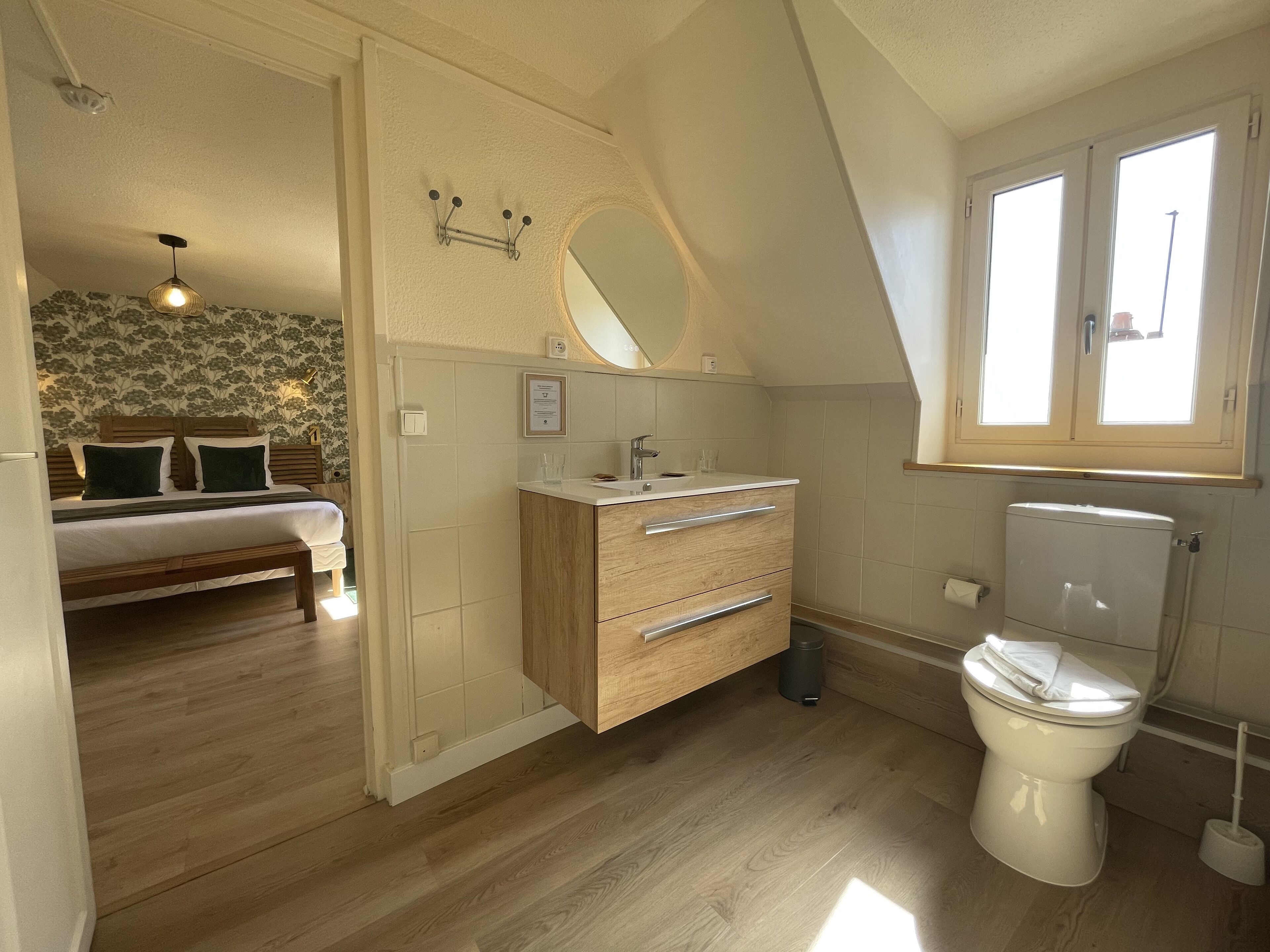 A bedroom with a bed, a wooden dresser, a bathroom with a toilet, and a window.