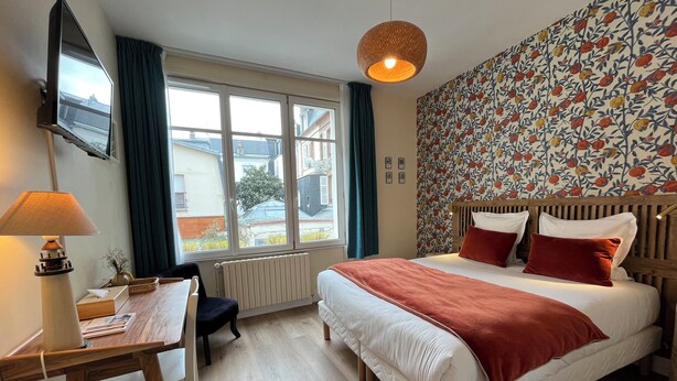 Een slaapkamer met een bed, een bureau, een stoel, een televisie, een raam en een behang met patroon.