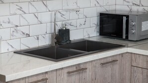 A kitchen with a double sink, a microwave, and a marble-tiled backsplash. - Spacious 2 level Brand New apt GTD3194 (Athens)