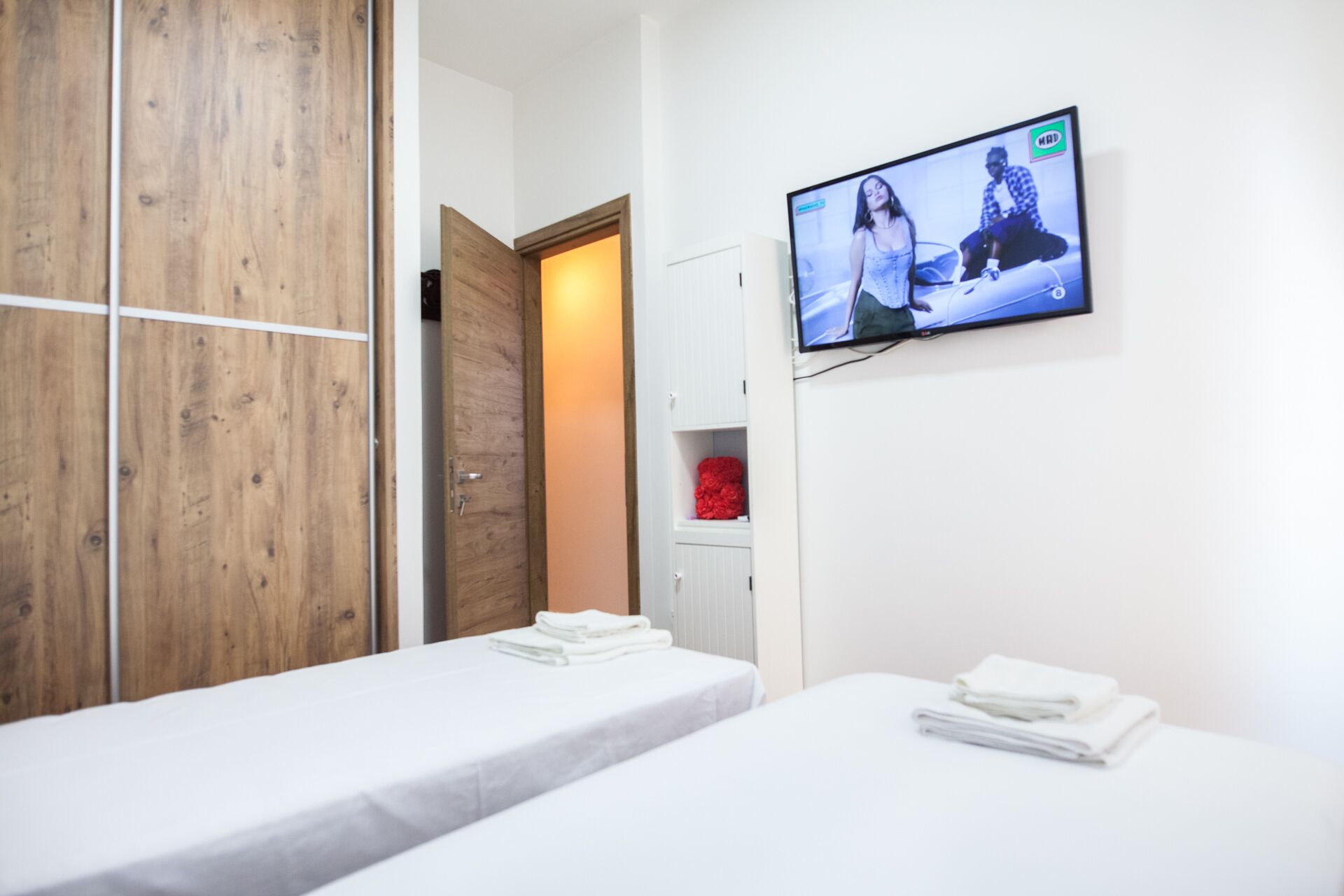 Une chambre d’hôtel avec deux lits simples, une armoire en bois, un téléviseur fixé au mur et un objet rouge à l’intérieur de l’armoire.