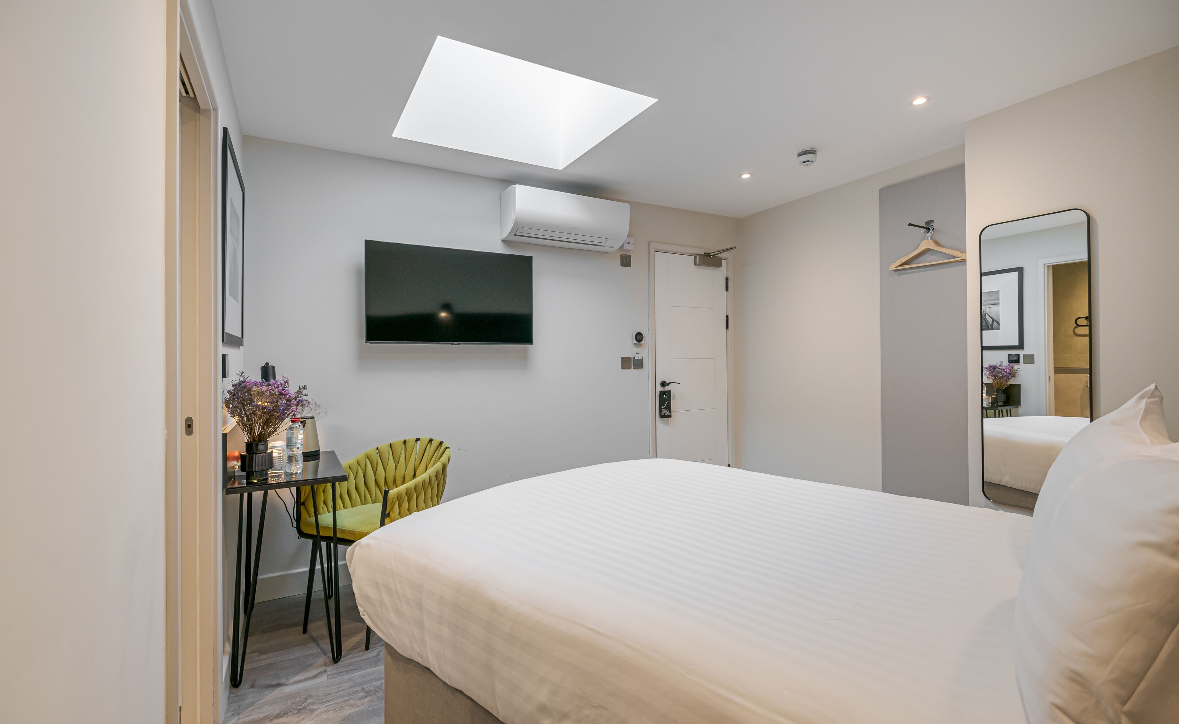 A modern hotel room with a bed, a desk, a chair, a TV, and a mirror.