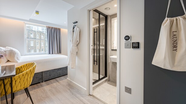Una habitación de hotel moderna con una cama, un escritorio, una silla, ducha y vistas a la ciudad.