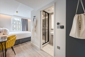 Una habitación de hotel moderna con una cama, un escritorio, una silla, ducha y vistas a la ciudad.