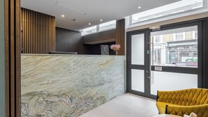 Un área de recepción con pared de mármol, pared de paneles de madera, una silla amarilla y un mostrador de recepción.